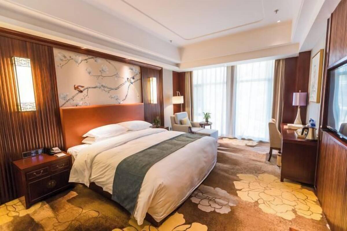 A hotel room with a large bed, a desk, a chair, a nightstand, and a wall-mounted TV.