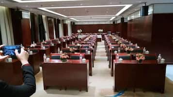 Une salle de conférence avec des rangées de tables et de chaises, équipée de microphones et de plaques nominatives.