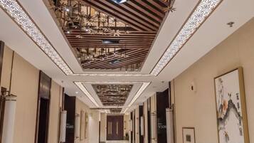 A hotel corridor with a patterned ceiling, doors labeled 'V305', and a framed artwork on the wall.