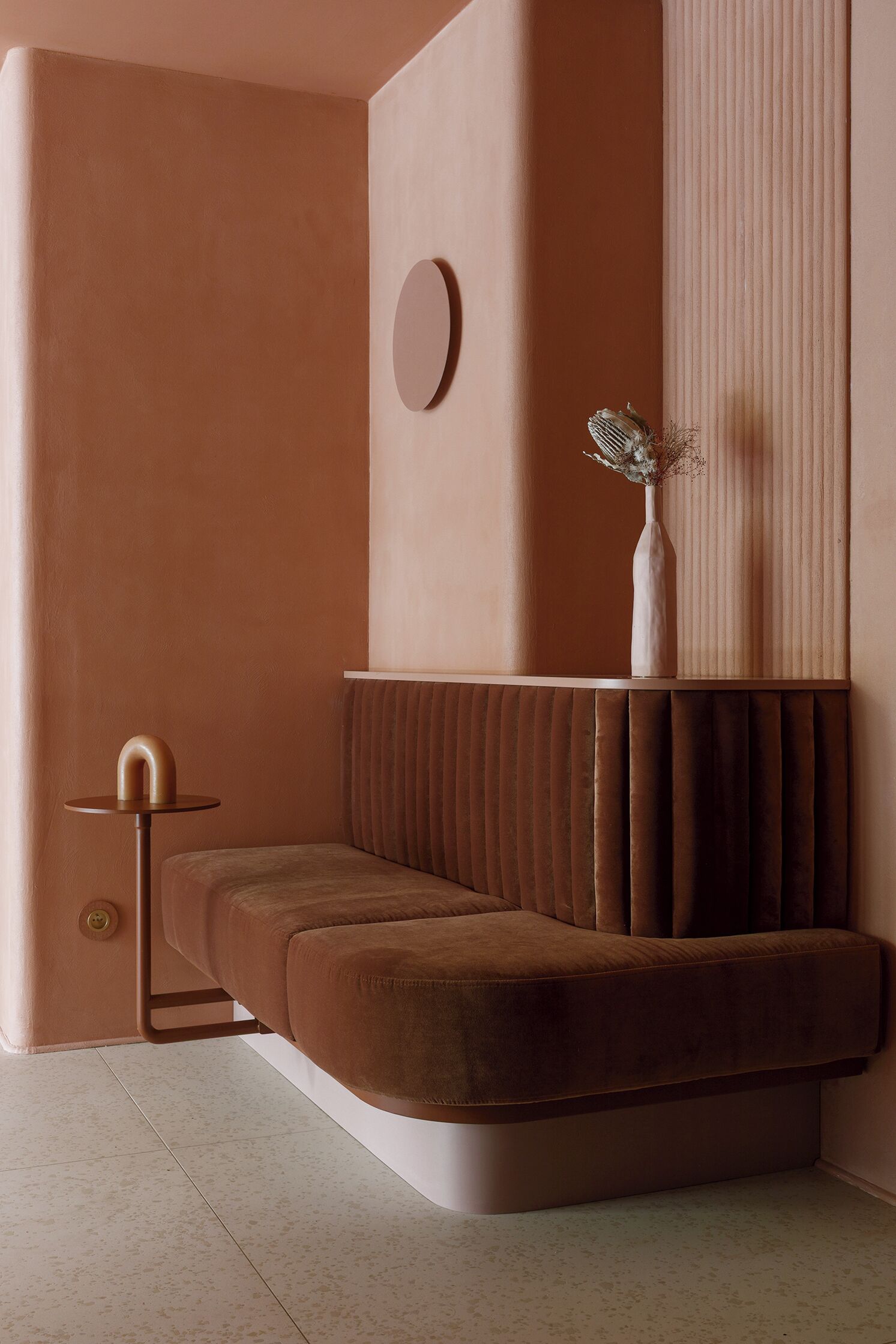 A modern, cozy room with a plush brown sofa, a small round table, and a decorative vase on a wall.