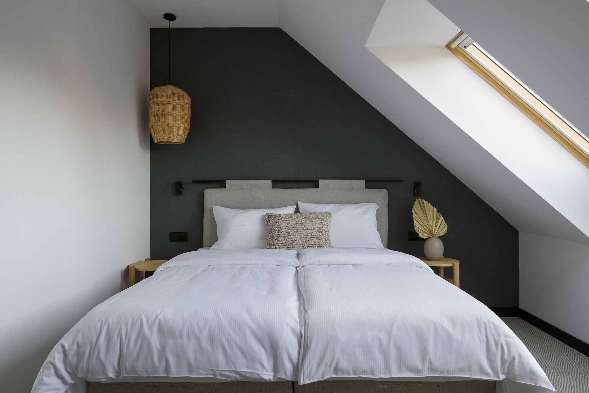 A modern bedroom with a bed, nightstands, and a skylight.