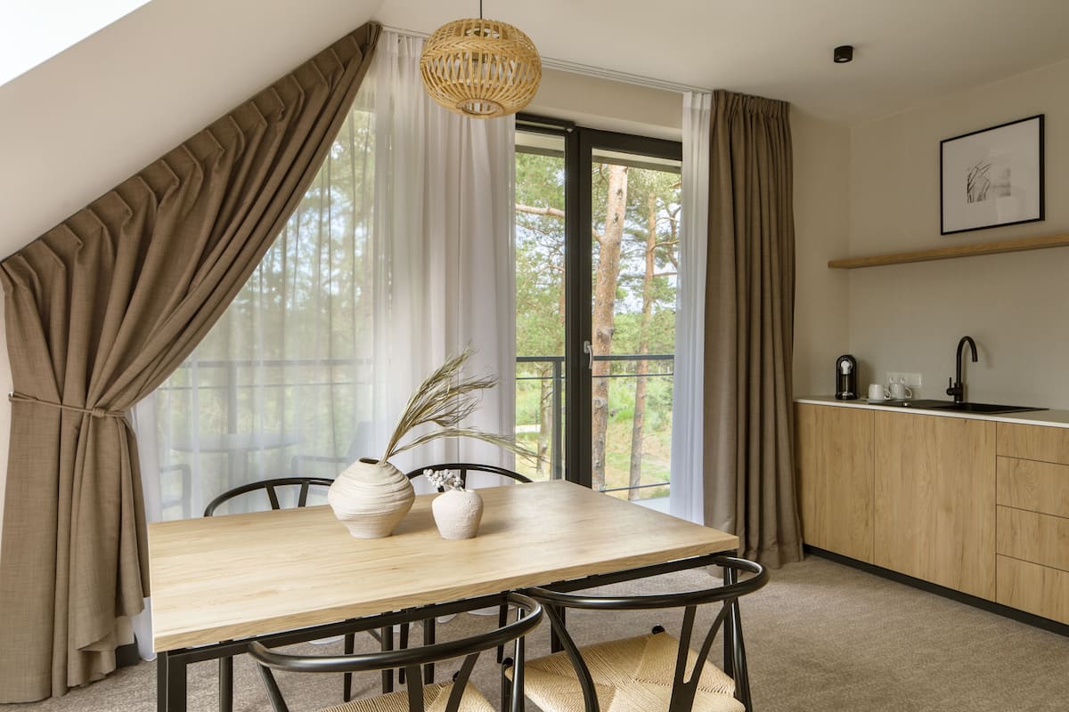 Eine moderne Küche mit Holztisch und -stühlen, einer Hängeleuchte und Blick auf Bäume durch das Fenster.