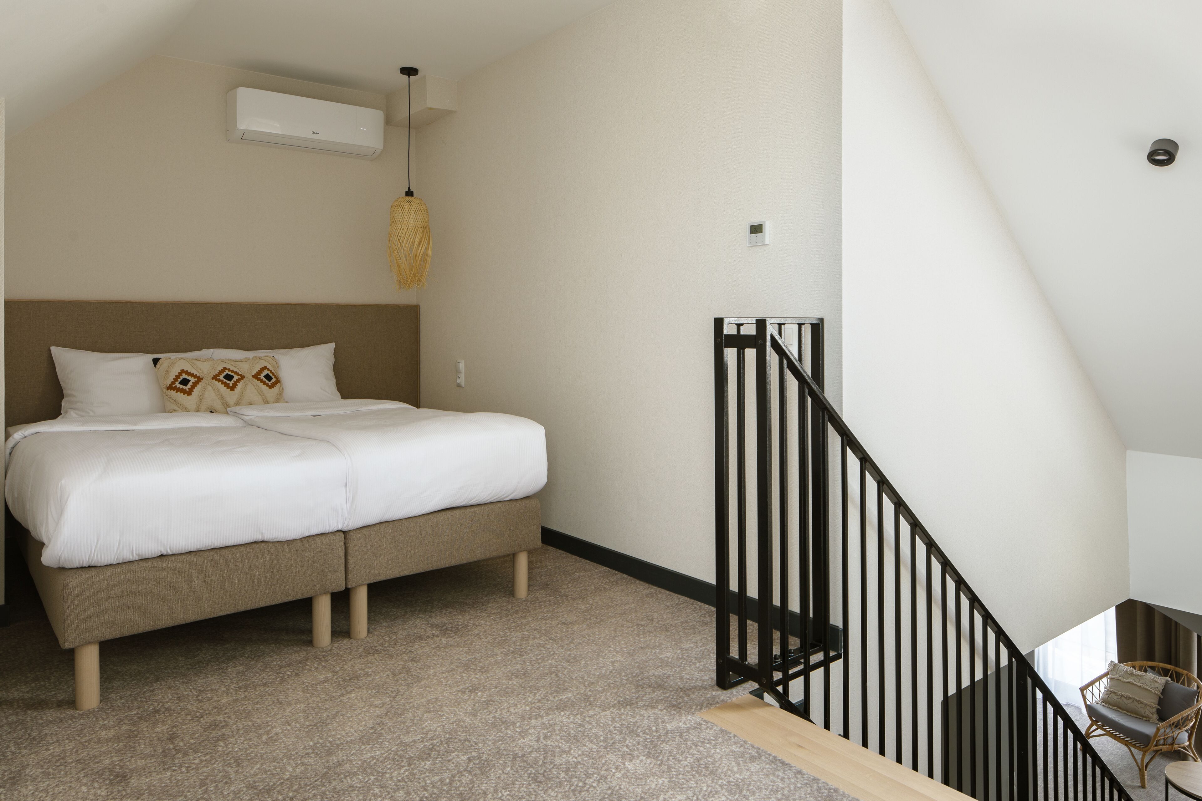 Un dormitorio con cama, lámpara colgante, escalera y una silla.