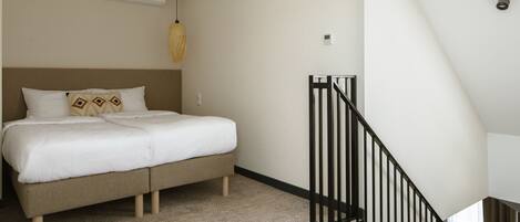 Un dormitorio con cama, lámpara colgante, escalera y una silla.