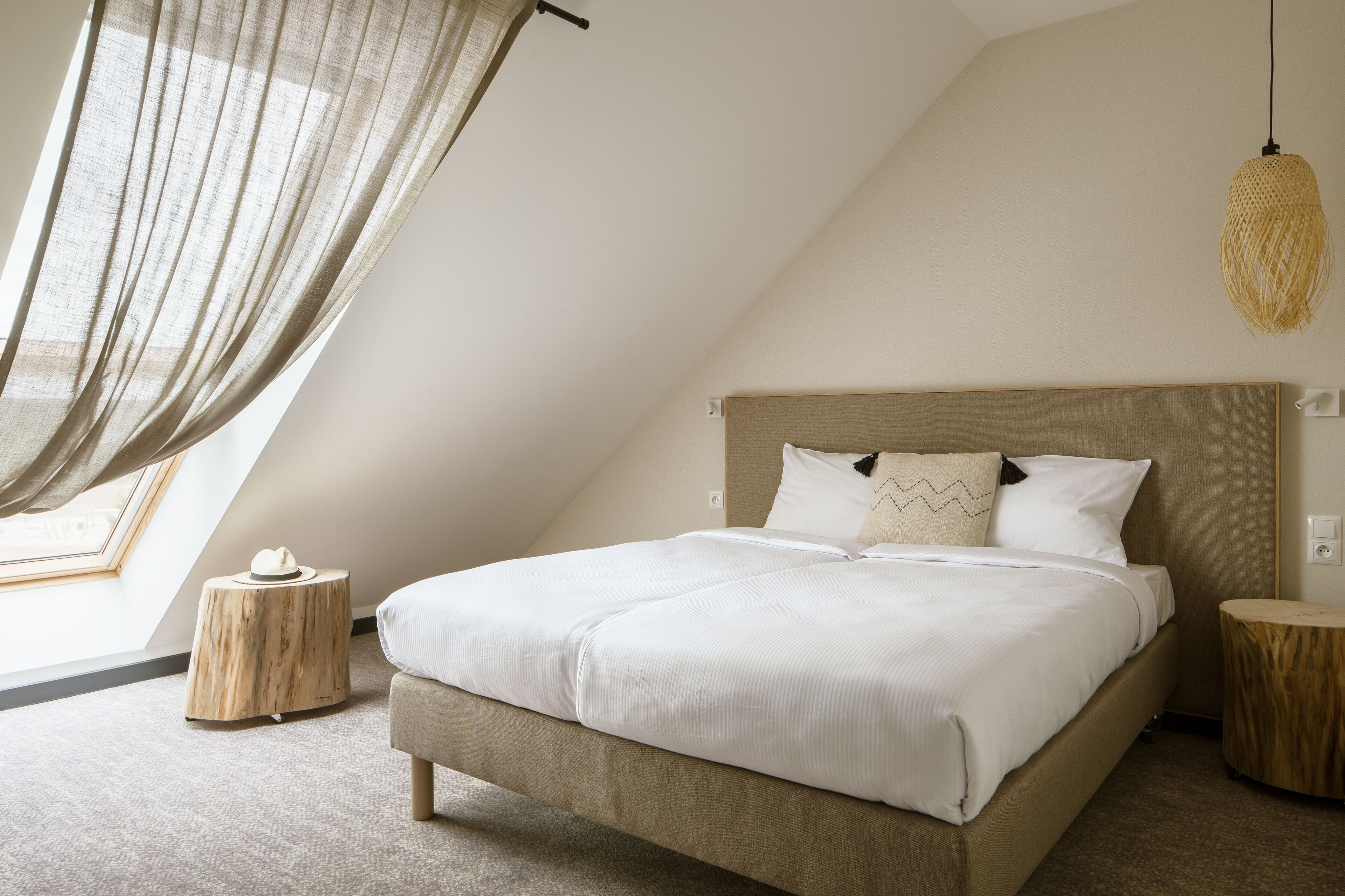 Ein Schlafzimmer mit einem Bett, einem Nachttisch, einer Lampe und einem Fenster mit Vorhängen.