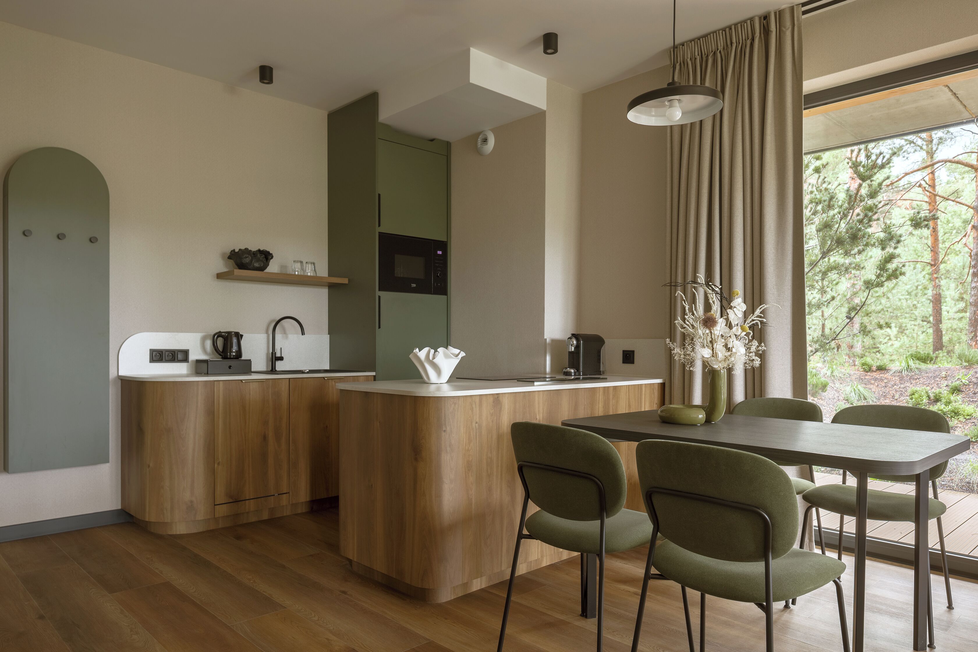A modern kitchen with a central island, wooden cabinets, and a dining area with green chairs.