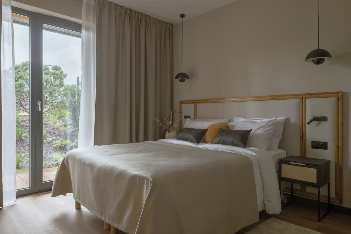 Ein Schlafzimmer mit einem großen Bett, einem Nachttisch, einer Lampe und Blick ins Grüne.