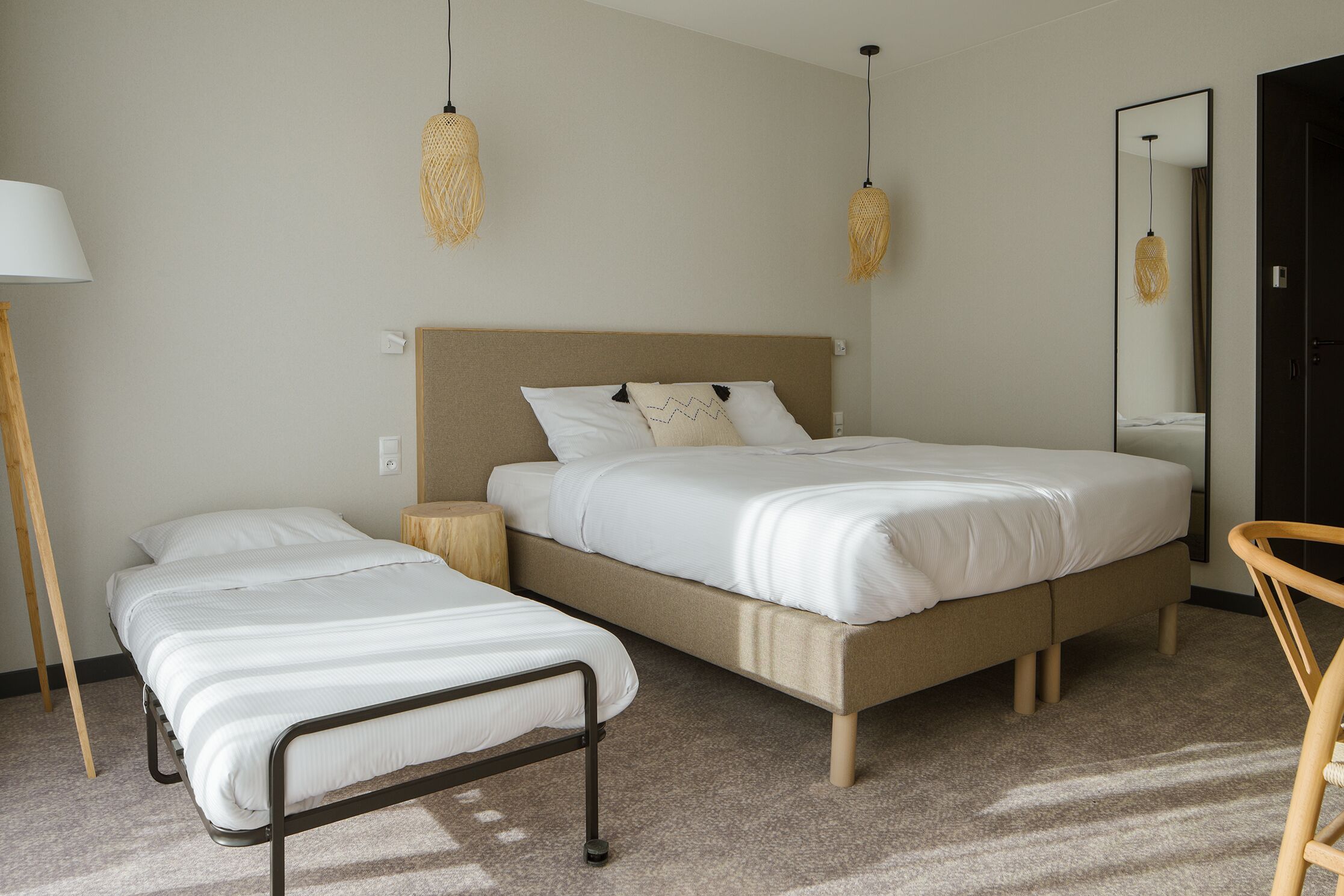 A bedroom with a large bed, a smaller bed, a bedside table, a lamp, and a mirror.
