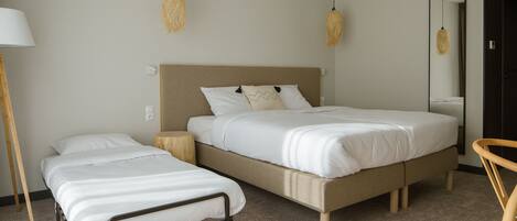 A bedroom with a large bed, a smaller bed, a bedside table, a lamp, and a mirror.