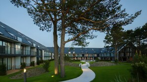 A modern building with a curved pathway, large trees, and a well-maintained lawn.