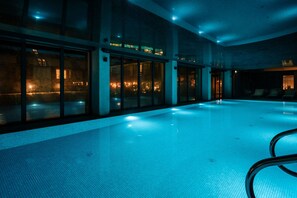An indoor swimming pool with clear glass walls, a tiled floor, and a seating area with lounge chairs. - Saltic Resort & SPA ŁEBA (Leba)