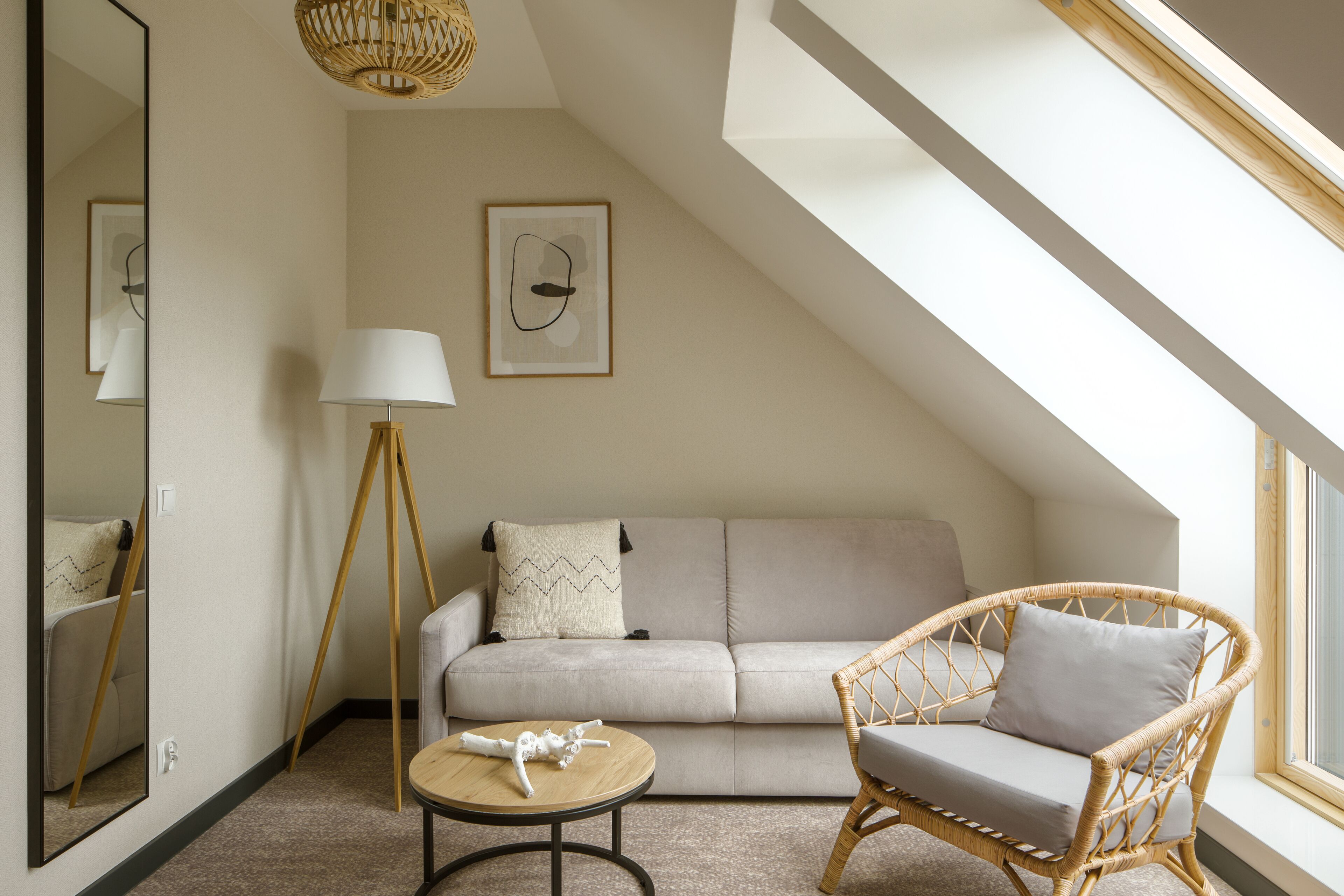 A cozy loft bedroom with a high ceiling, a rattan chair, a sofa, a round table, and a large mirror.
