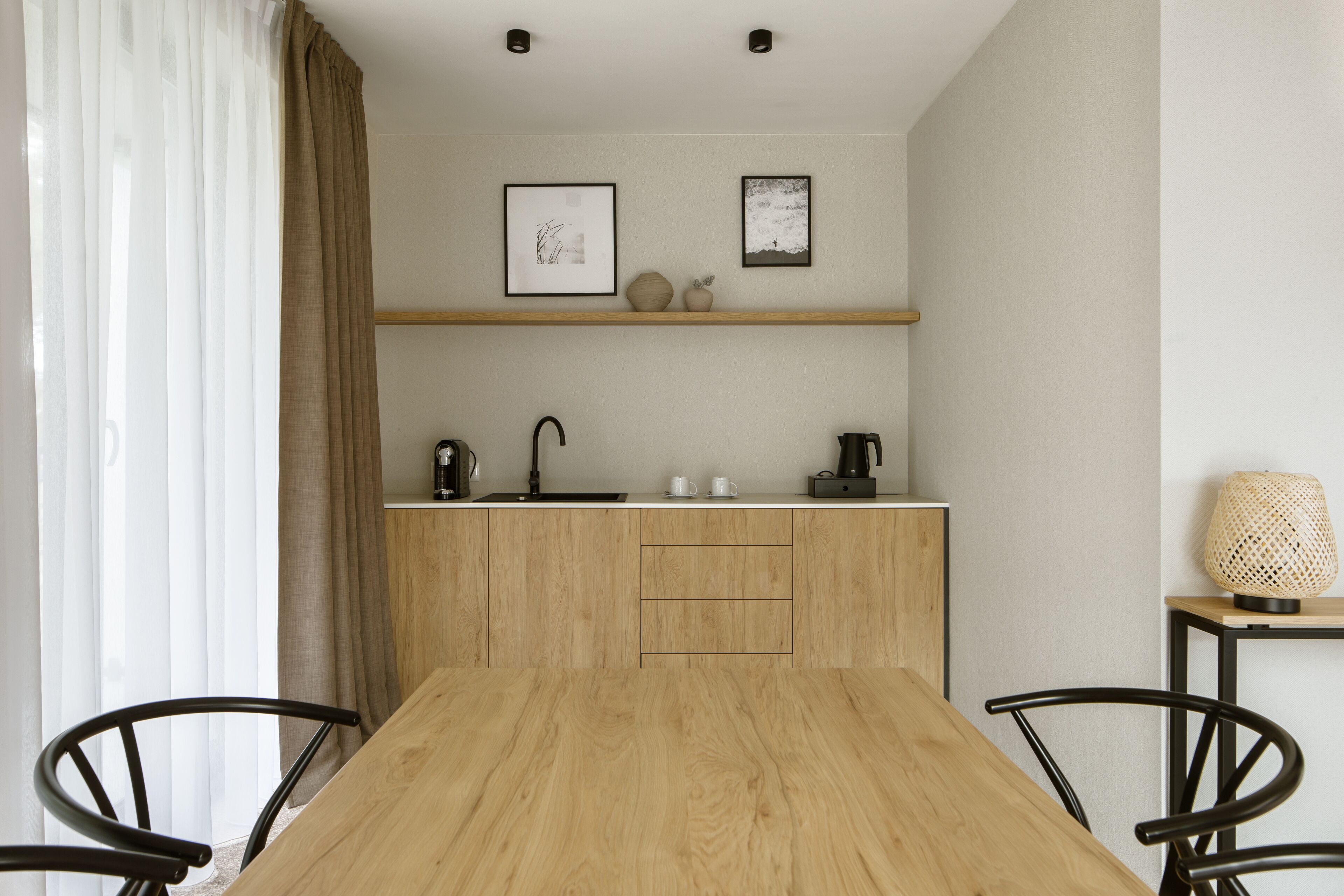 Una cocina moderna con una mesa y sillas de madera, un lavamanos y una estantería con objetos decorativos.