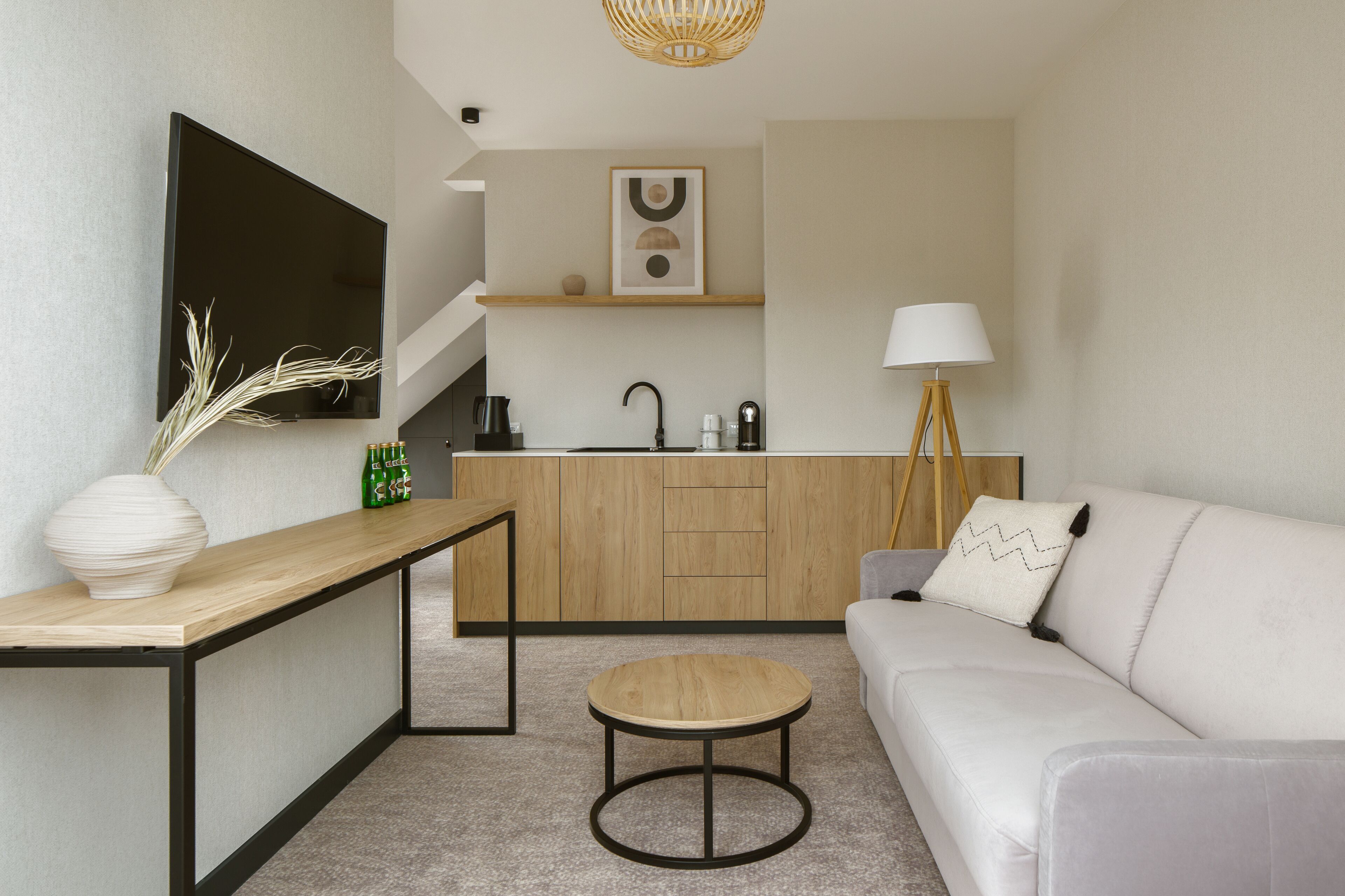 A modern living room with a sofa, a coffee table, a TV, a kitchen area with a sink and cabinets, and a staircase.