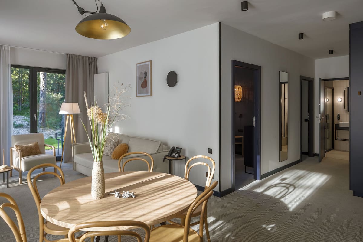 Ein modernes Wohnzimmer mit einem runden Holztisch, beigefarbenen Sofas und einem großen Fenster mit Vorhängen.
