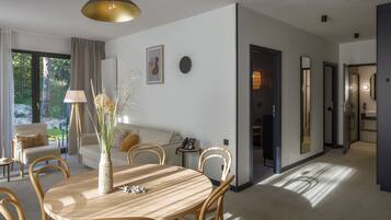 A modern living room with a round wooden table, beige sofas, and a large window with curtains.
