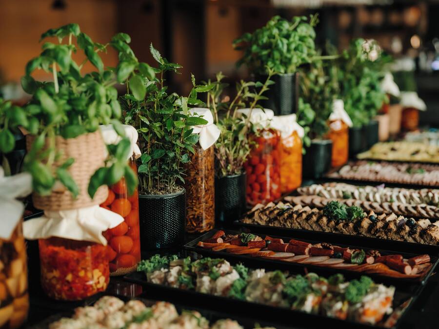 A buffet with various food items and potted plants.