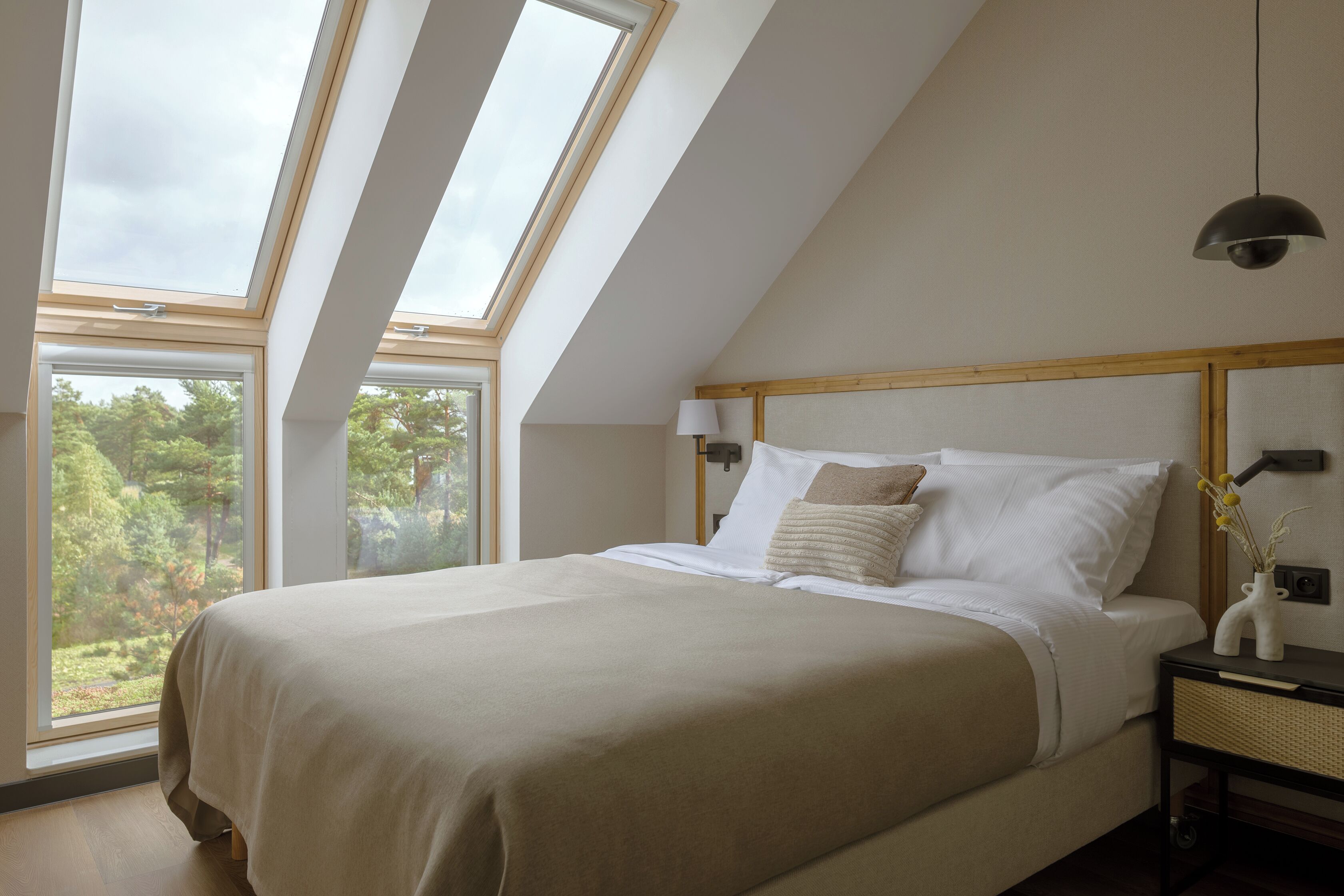 Een slaapkamer met een groot bed, dakramen en uitzicht op bomen.