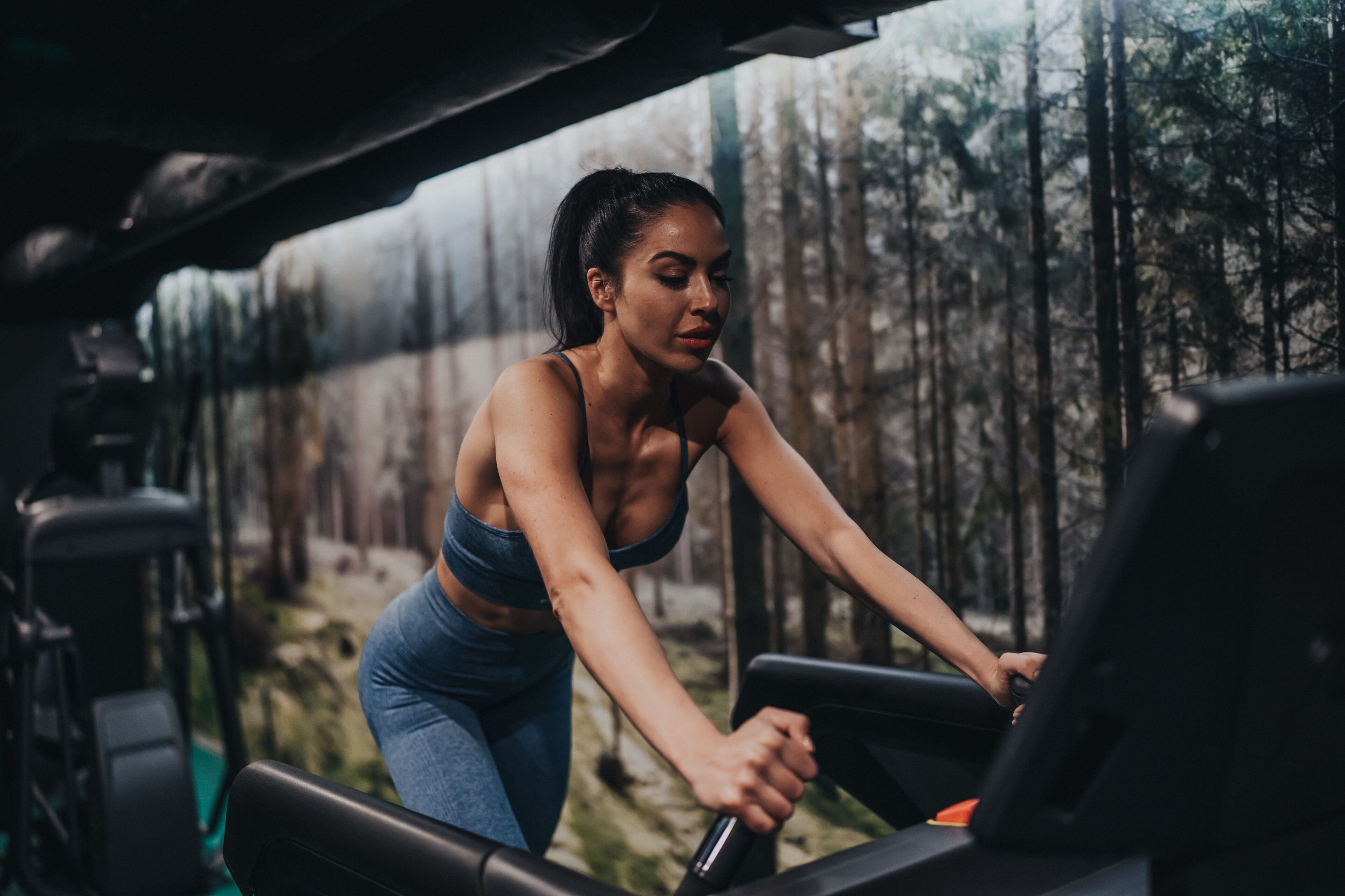 A woman exercising on a treadmill in a gym with a forest view.