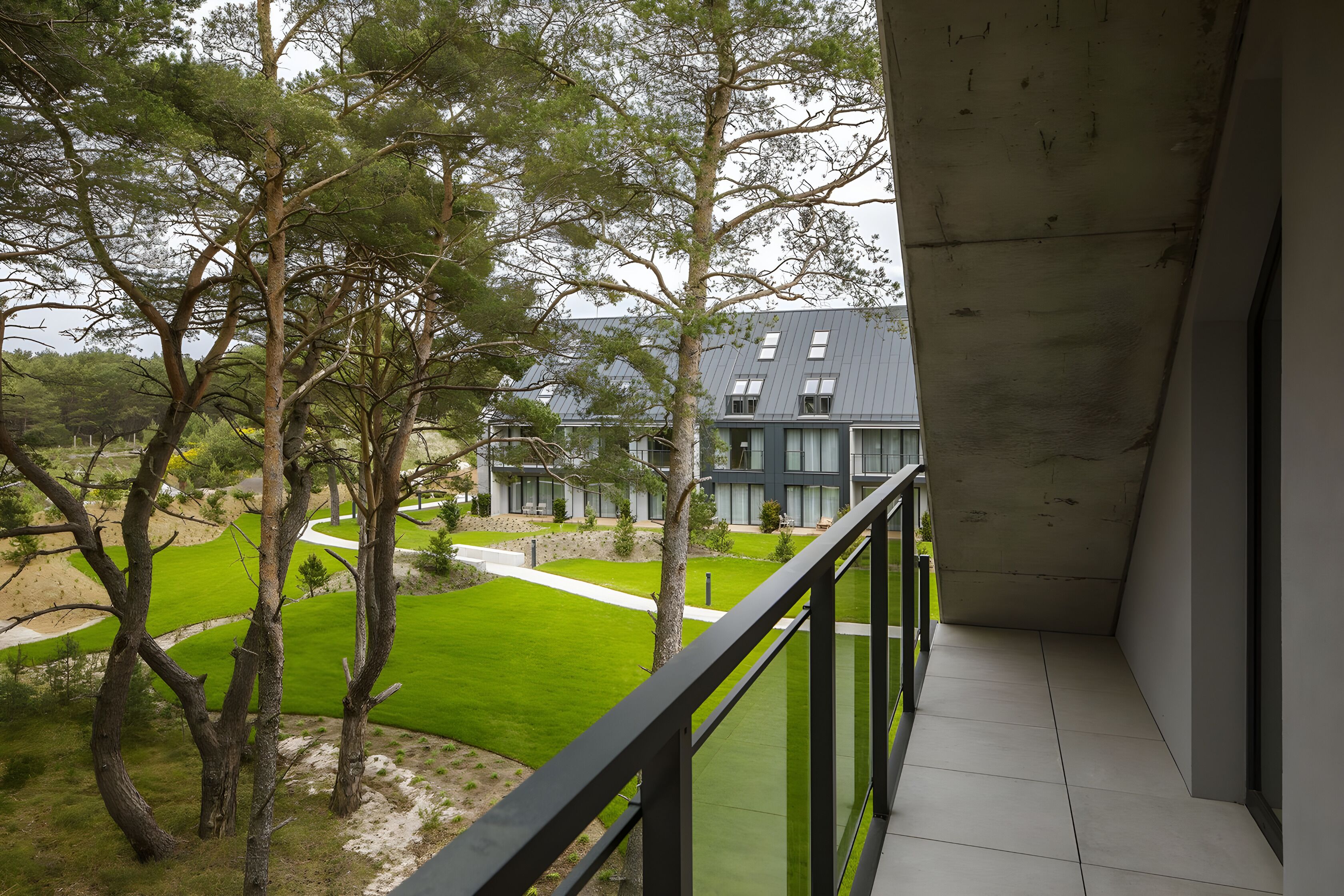 Un balcon donnant sur une pelouse verdoyante, des arbres et un bâtiment dont le toit est gris.