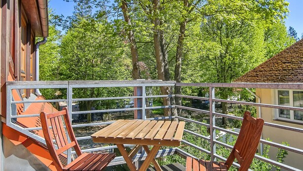 Eine Holzterrasse mit zwei Holzstühlen und einem Tisch, mit Blick auf ein Gewässer und Bäume.