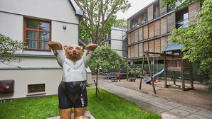 Eine Statue eines Bären in einem Innenhof mit Spielplatz, einem Gebäude mit großen Fenstern und einem Baum.
