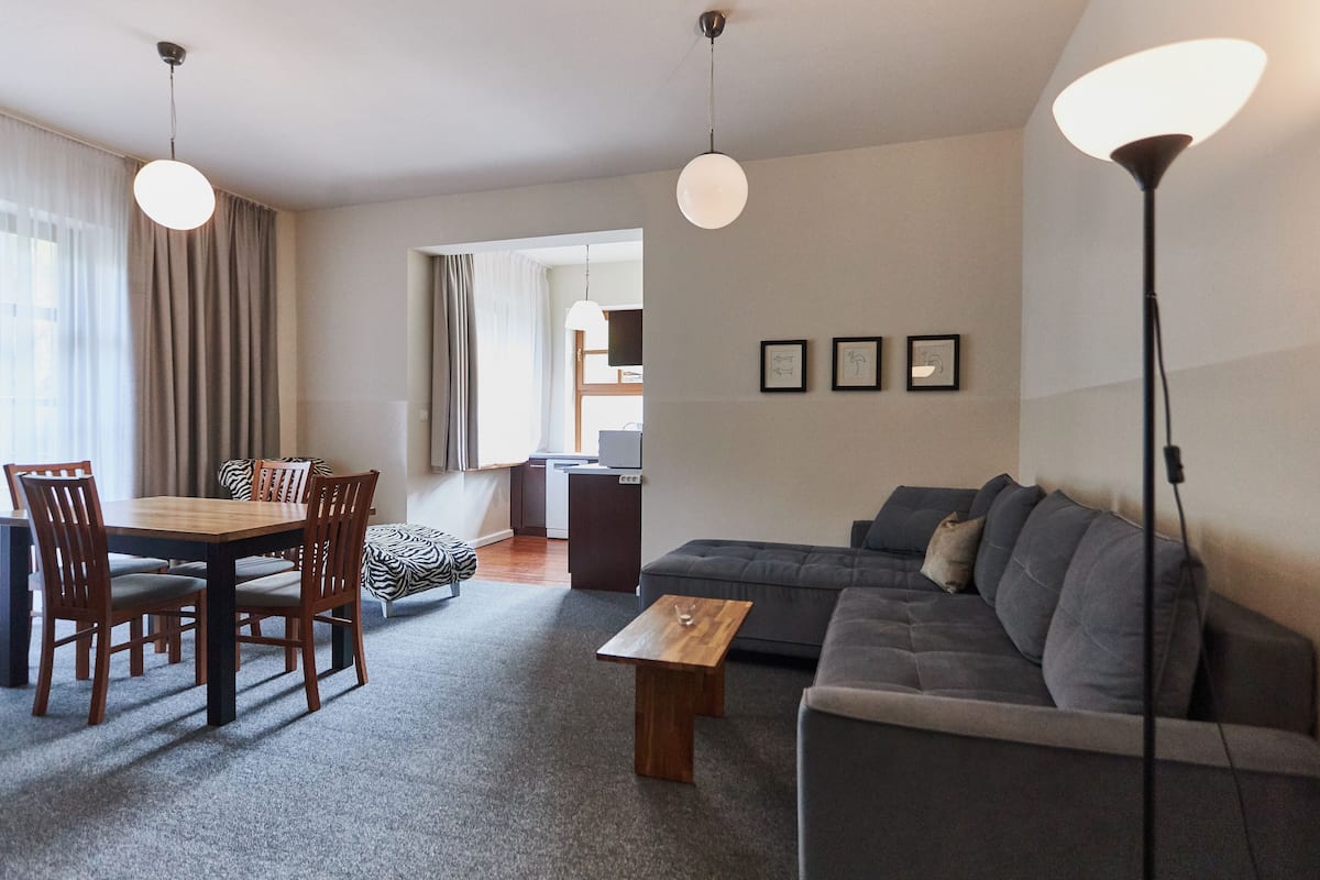 A modern living room with a dining area, grey sofa, wooden dining table, and pendant lights.