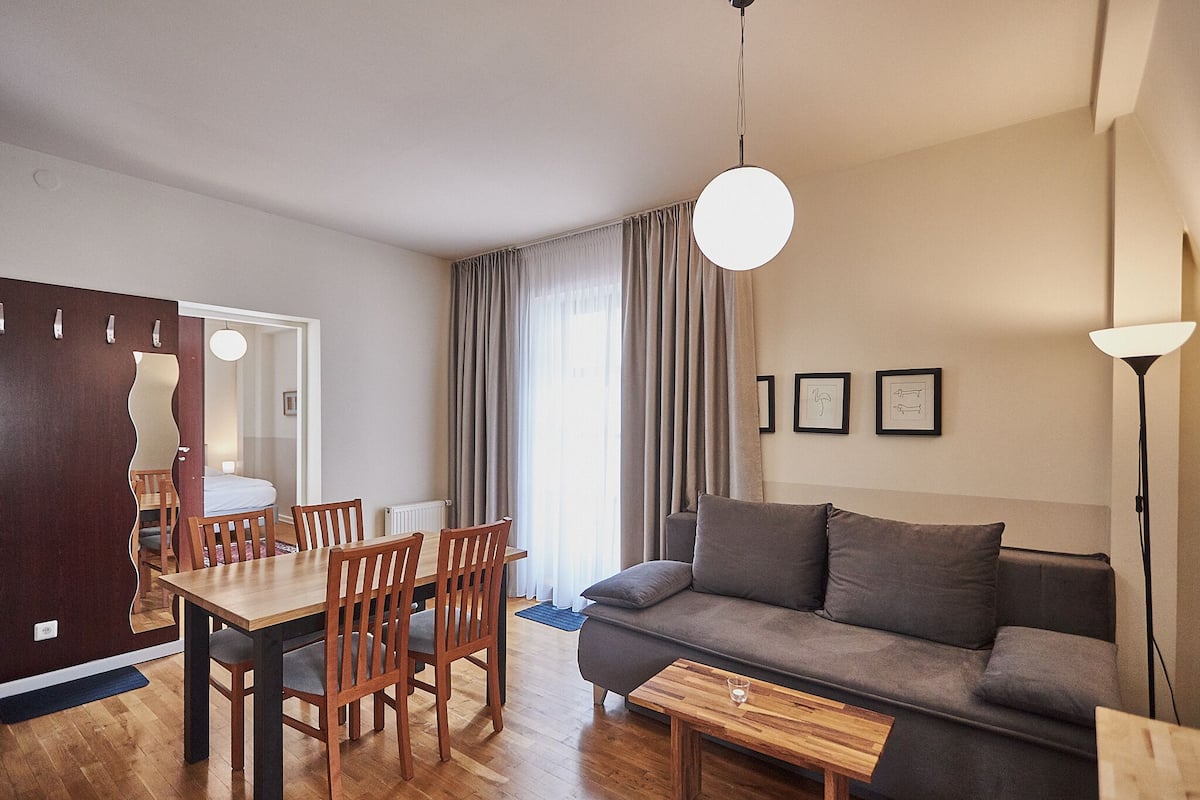 A modern living room with a sofa, dining table, chairs, and a hanging light fixture.