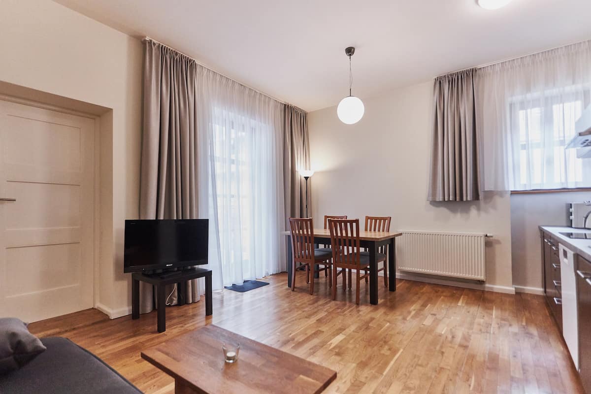 A modern living room with a flat-screen TV, wooden dining table, and chairs.