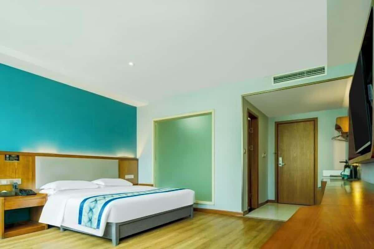 A hotel room with a bed, bedside table, TV, and a door leading to another room.