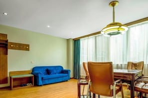 Een woonkamer met een blauwe bank, een houten bankje, een eettafel met stoelen en een plafondlamp.