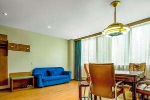 Sala de estar com sofá azul, um banco de madeira, mesa de jantar com cadeiras e luminária no teto.