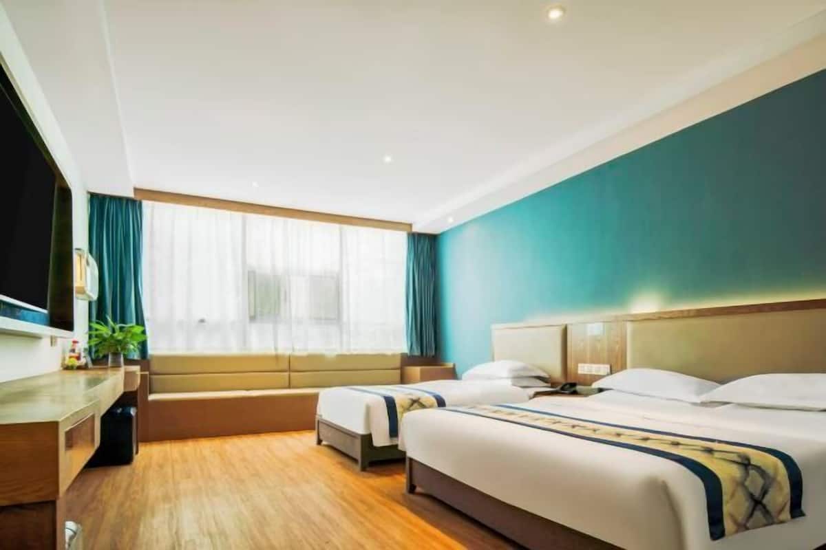A hotel room with two beds, a wooden desk, a television, and a window with curtains.