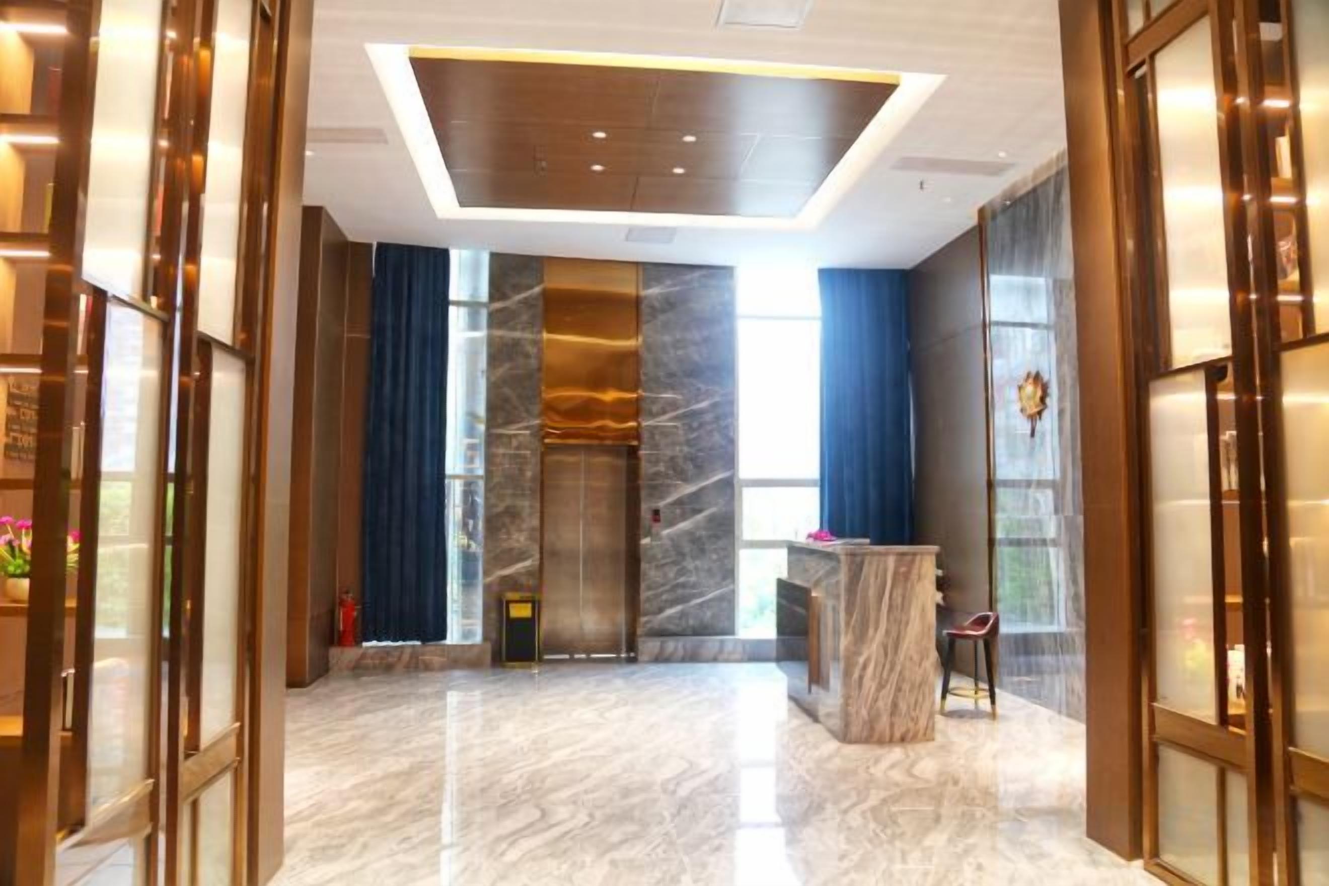 A lobby with a marble floor, a reception desk, and a large glass elevator.