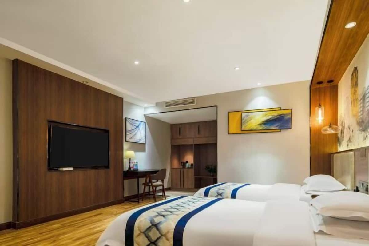 A hotel room with a bed, a desk, a television, and artwork on the walls.