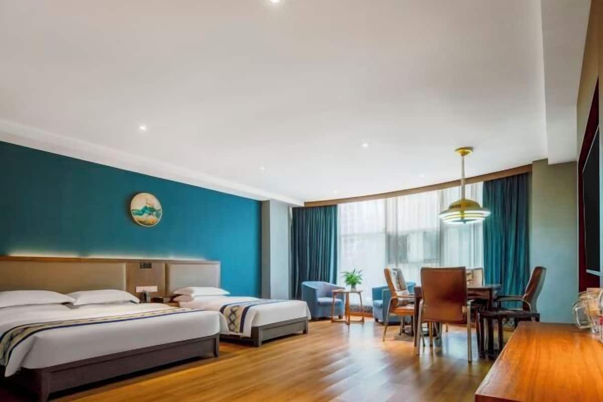 A hotel room with two beds, a dining area with chairs and a table, and a large window with curtains.