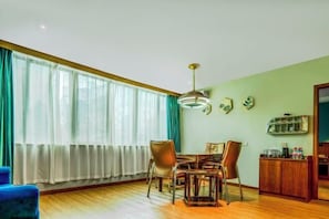 Een eetruimte met een houten tafel en stoelen, een hanglamp en uitzicht op een raam met gordijnen.