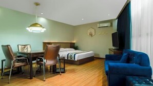 A hotel room with a bed, a blue sofa, a dining table with chairs, a television, and a ceiling light fixture. - HengYangYi’nian Yuexiang Hotel (Hengyang)