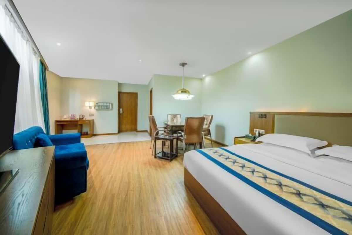 A hotel room with a bed, a desk with chairs, a small table, and a TV.