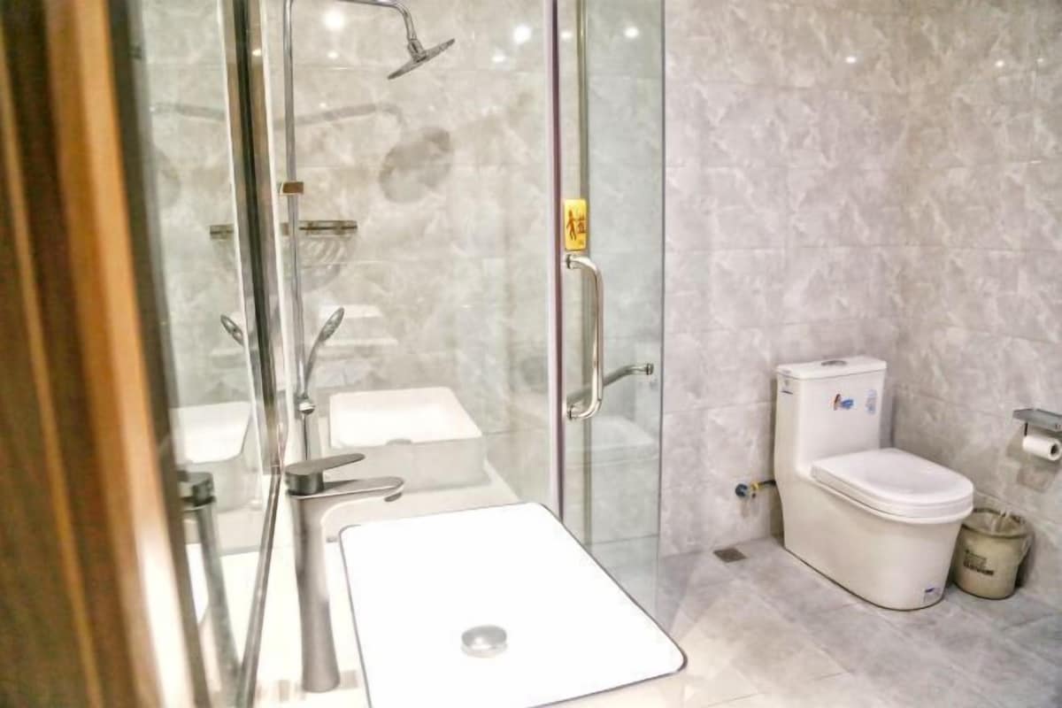 Een moderne badkamer met een douchecabine van glas, een witte wastafel en een toilet.