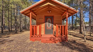 A wooden cabin with a porch, surrounded by trees. - Hot Tub Hideaway in Pinetop: Bring Your Pet! (Pinetop-Lakeside)