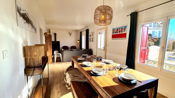 A dining area with a long wooden table set for a meal, a hanging light fixture, and a view of the outside through a window. - Large family house sleeping 16 in the mountains (Font-Romeu-Odeillo-Via)