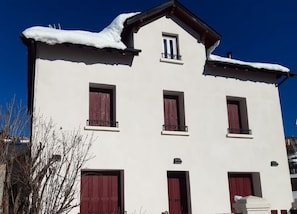 A two-story building with a white facade, red shutters, and snow on the roof.