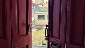 A view through open wooden doors to a balcony with a clear blue sky, a church tower, and a fenced area. - Large family house sleeping 16 in the mountains (Font-Romeu-Odeillo-Via)