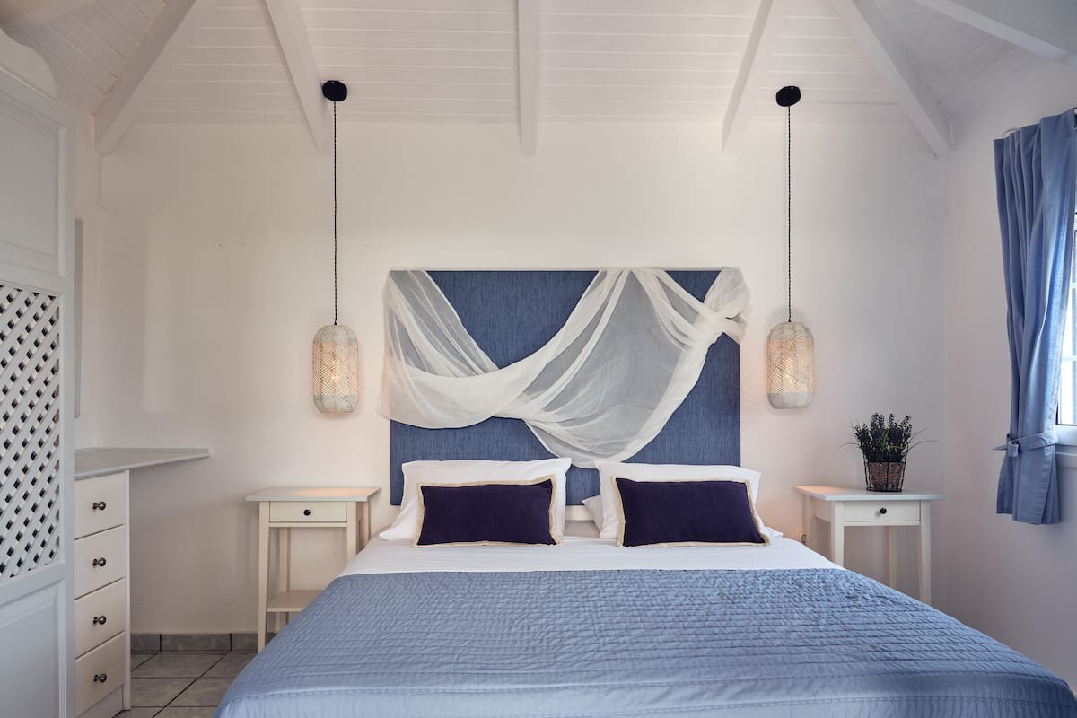 A bedroom with a large bed, two bedside tables, a nightstand, a wardrobe, and a window with curtains.