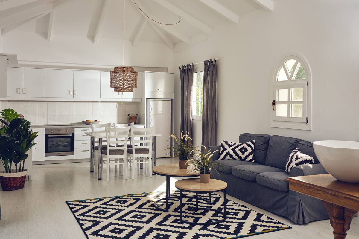 A spacious living room with a grey sofa, a round wooden coffee table, and a dining area with white chairs and a white table.