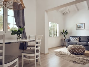 A bright room with a dining table, chairs, a sofa, and a window.