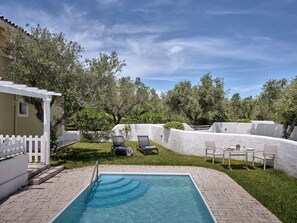 En swimmingpool med ett vitt staket, solstolar och en pergola.