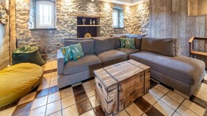 A cozy living room with a stone wall, wooden beams, a grey sectional sofa, and a wooden chest of drawers. - Holiday home in Melreux-Hotton with sauna (Melreux-Hotton)