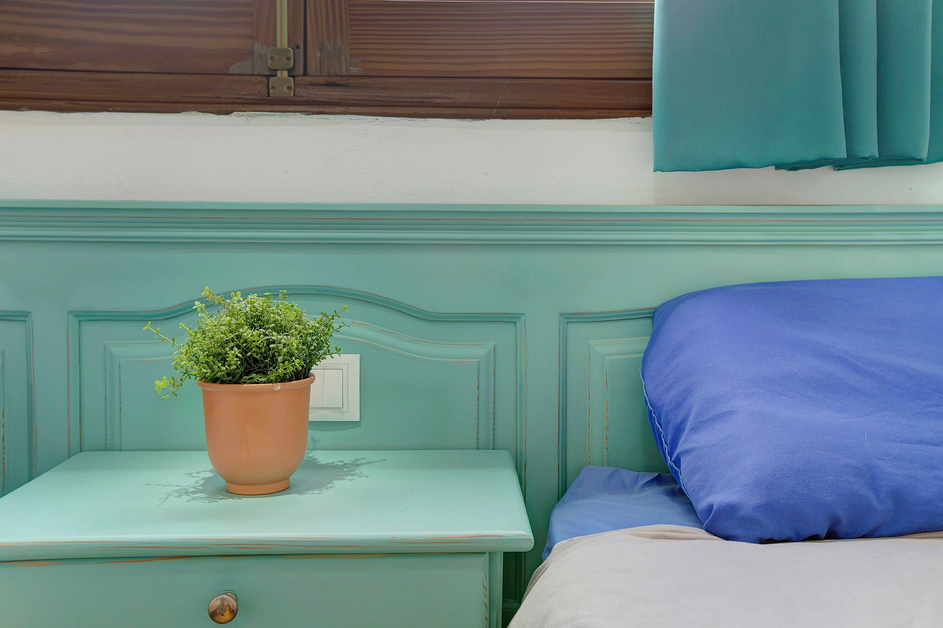A teal-colored bed with a blue pillow and a nightstand with a potted plant.